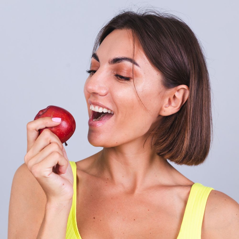 mujer deportiva encuentra pared gris satisfecha resultados entrenamiento fisico dieta sosteniendo bascula usa parte superior polainas sostiene manzana.jpg